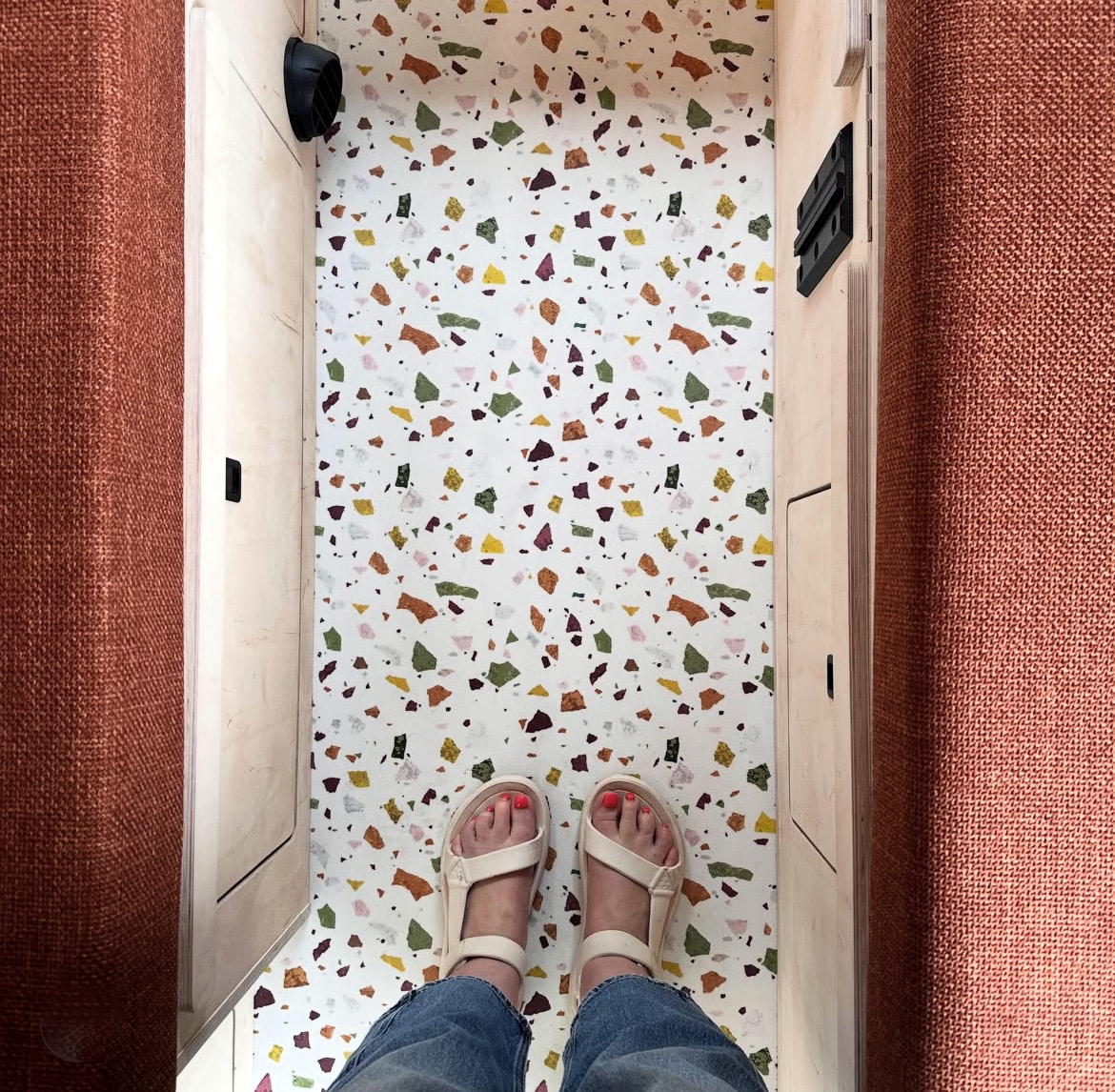 Patterned vinyl flooring in a fitted campervan with flooring and feet visible in the aisle