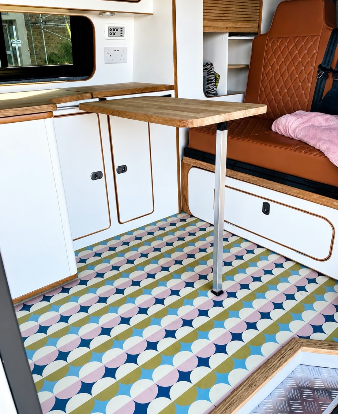Patterned vinyl flooring in a campervan with white cabinetry and leather seating